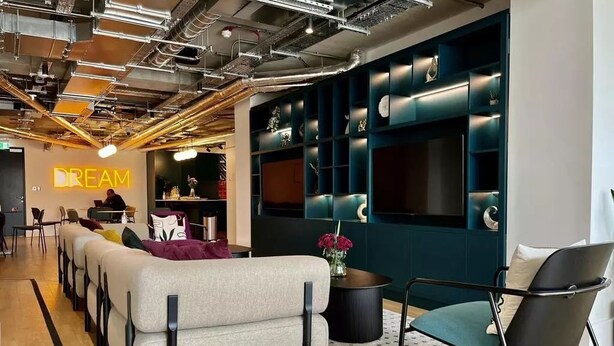 Un espace de détente moderne comprenant un canapé, des fauteuils et un écran fixé au mur.