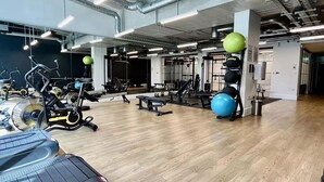 Une salle de sport équipée de matériel d’exercice, dotée d’un plancher en bois et de tuyaux apparents au plafond.