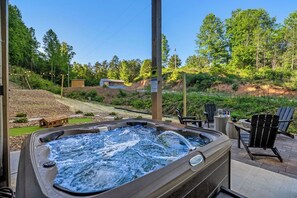 Un bain à remous avec une terrasse en bois, des chaises d’extérieur et une vue sur une colline boisée.