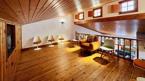 A wooden-floored room with a high ceiling, a fireplace, and a balcony with a railing. - Calma CostaBravaSi - Terrace, garden, Barbecue (Santa Cristina d'Aro)