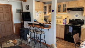 Ett kompakt bostadsutrymme med ett kök, en matplats med barstolar, en tv och en mysig sittgrupp med en filt.