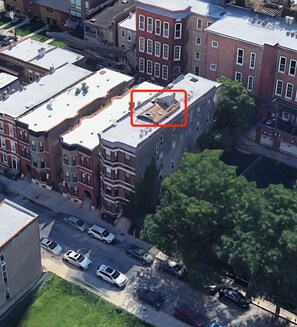 An aerial view of a residential area with multi-story buildings, a street with parked cars, and a large tree.