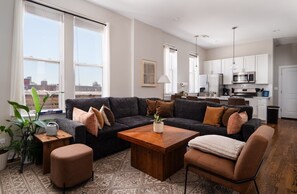 Ein modernes Wohnzimmer mit einem Ecksofa, einem Couchtisch aus Holz und einem gemusterten Teppich.