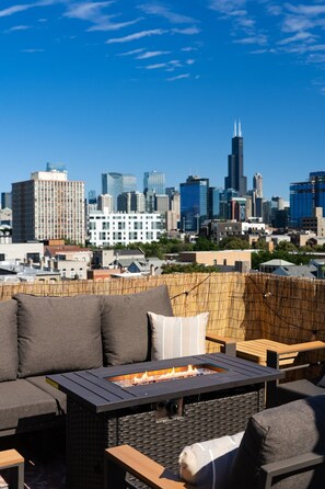 A rooftop patio with a fire feature, seating, and a city skyline view.
