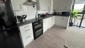 A modern kitchen with white cabinets, a black refrigerator, a stove, and a microwave. - Sky View Apartment (Barking)