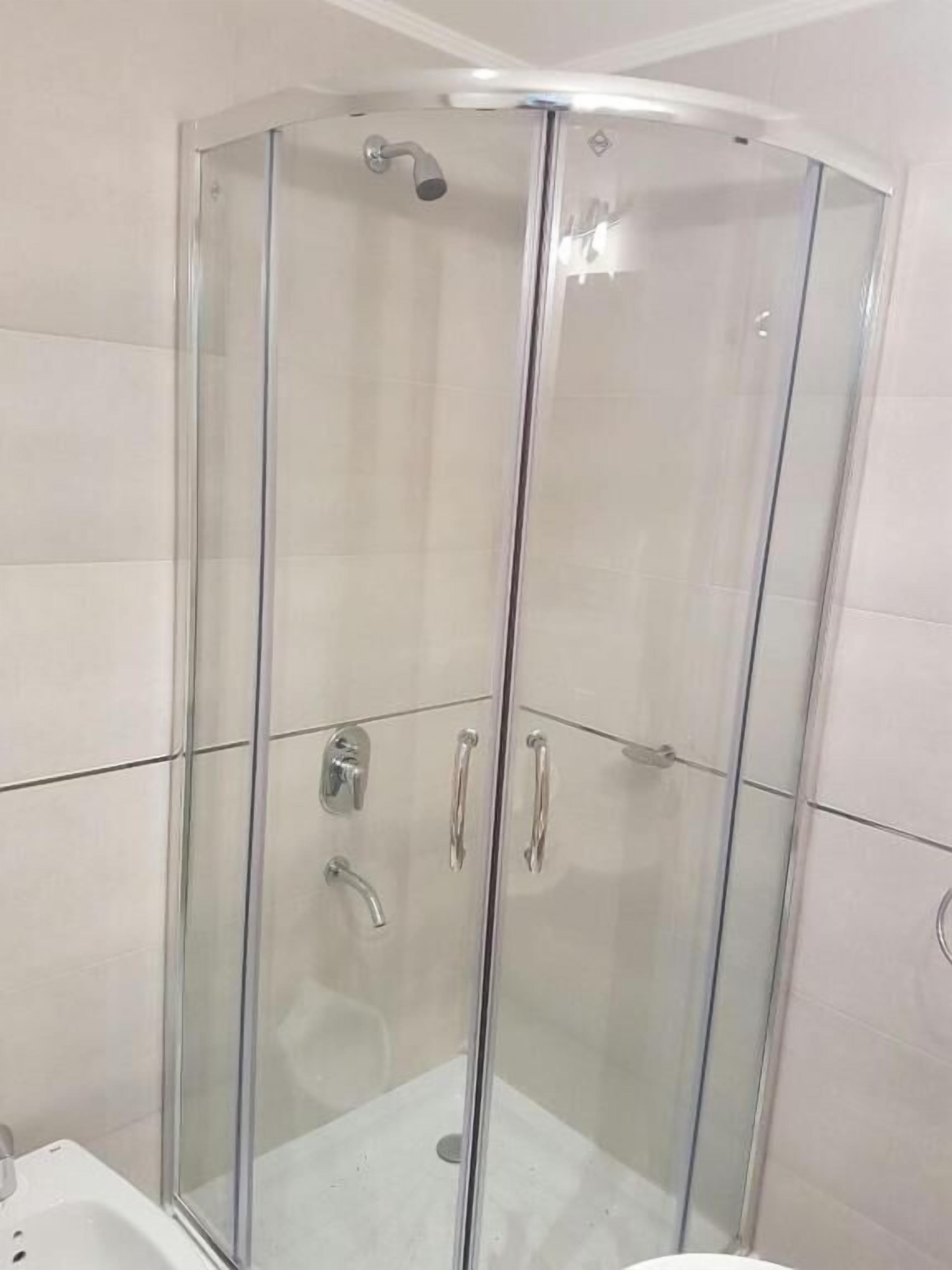 A glass-enclosed shower stall with a handheld showerhead and a wall-mounted faucet.