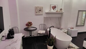 A modern bathroom with a freestanding bathtub, a small round table with a vase of flowers, a chair, and a shelf with decorative items. - Apartmán s vlastným parkovaním a terasou. 5 minút od centra a starého prístavu! (Genova)