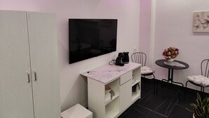 A modern room with a flat-screen TV mounted on the wall, a white cabinet with drawers, a small round table with chairs, and a potted plant. - Apartmán s vlastným parkovaním a terasou. 5 minút od centra a starého prístavu! (Genova)