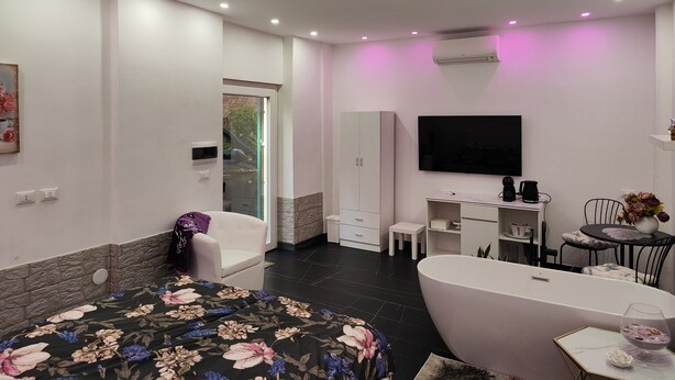 A modern bedroom with a large bed, a bathtub, a TV, and a desk area. - Apartmán s vlastným parkovaním a terasou. 5 minút od centra a starého prístavu! (Genova)