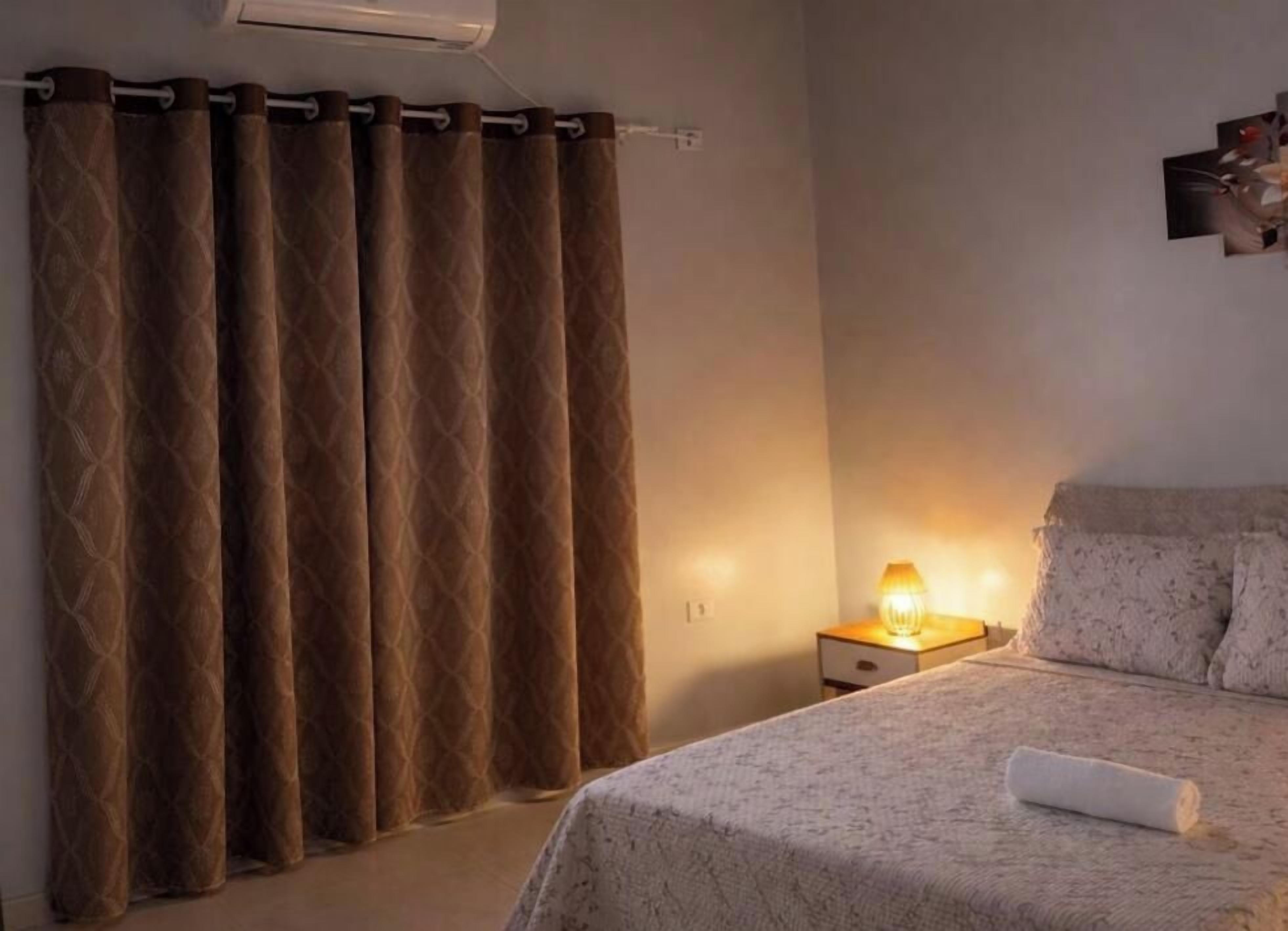 Ein Schlafzimmer mit einem Bett, einem Nachttisch mit Lampe und einem Vorhang.
