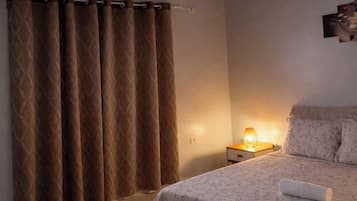 Ein Schlafzimmer mit einem Bett, einem Nachttisch mit Lampe und einem Vorhang.