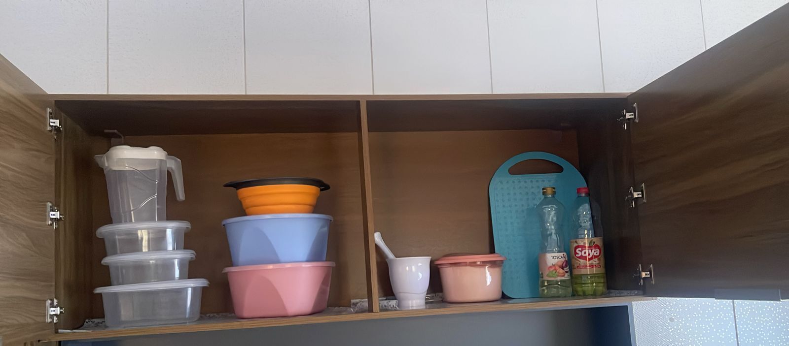 Un armario de cocina con recipientes de plástico, un filtro de agua, una tabla de cortar y utensilios de cocina.