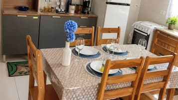A dining area with a table set for four, wooden chairs, a vase with flowers, and a kitchen in the background.