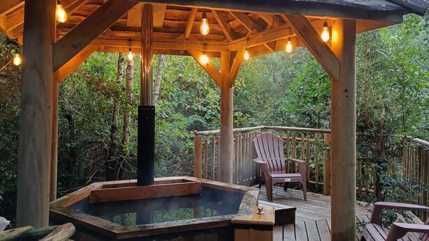 A wooden gazebo with a hot tub, wooden deck, and a chair. - Dome in green Patagonia with view and access to the Petrohue River, Tinas Calientes. (Cochamo)