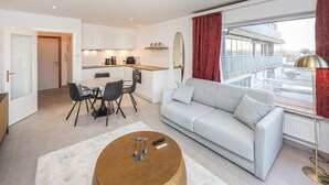 Eine moderne Wohnung mit Essbereich, Küchenzeile und Wohnzimmer mit Sofa und großem Fenster.