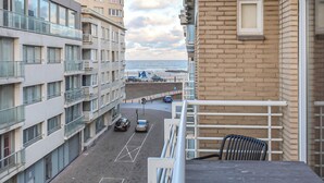 Blick vom Balkon auf eine Straße mit parkenden Autos, einen Fußweg und ein Gebäude mit Ziegelaußenwand.