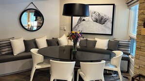 Ein modernes Wohnzimmer mit einem runden schwarzen Tisch, weißen Stühlen, einem grauen Sofa mit Kissen, einem runden Spiegel und einem großen schwarz-weißen Kunstwerk an der Wand.