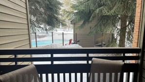 Ein Balkon mit Blick auf eine verschneite Landschaft, ein Schwimmbad und ein Zaun.