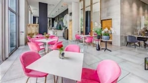 Un espace repas moderne avec des chaises roses et une table blanche, de grandes fenêtres et un sol carrelé, sobre et élégant.