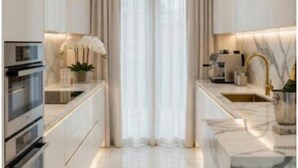 Une cuisine moderne dotée de plans de travail en marbre, d’appareils électroménagers en acier inoxydable et d’un îlot central avec un évier.