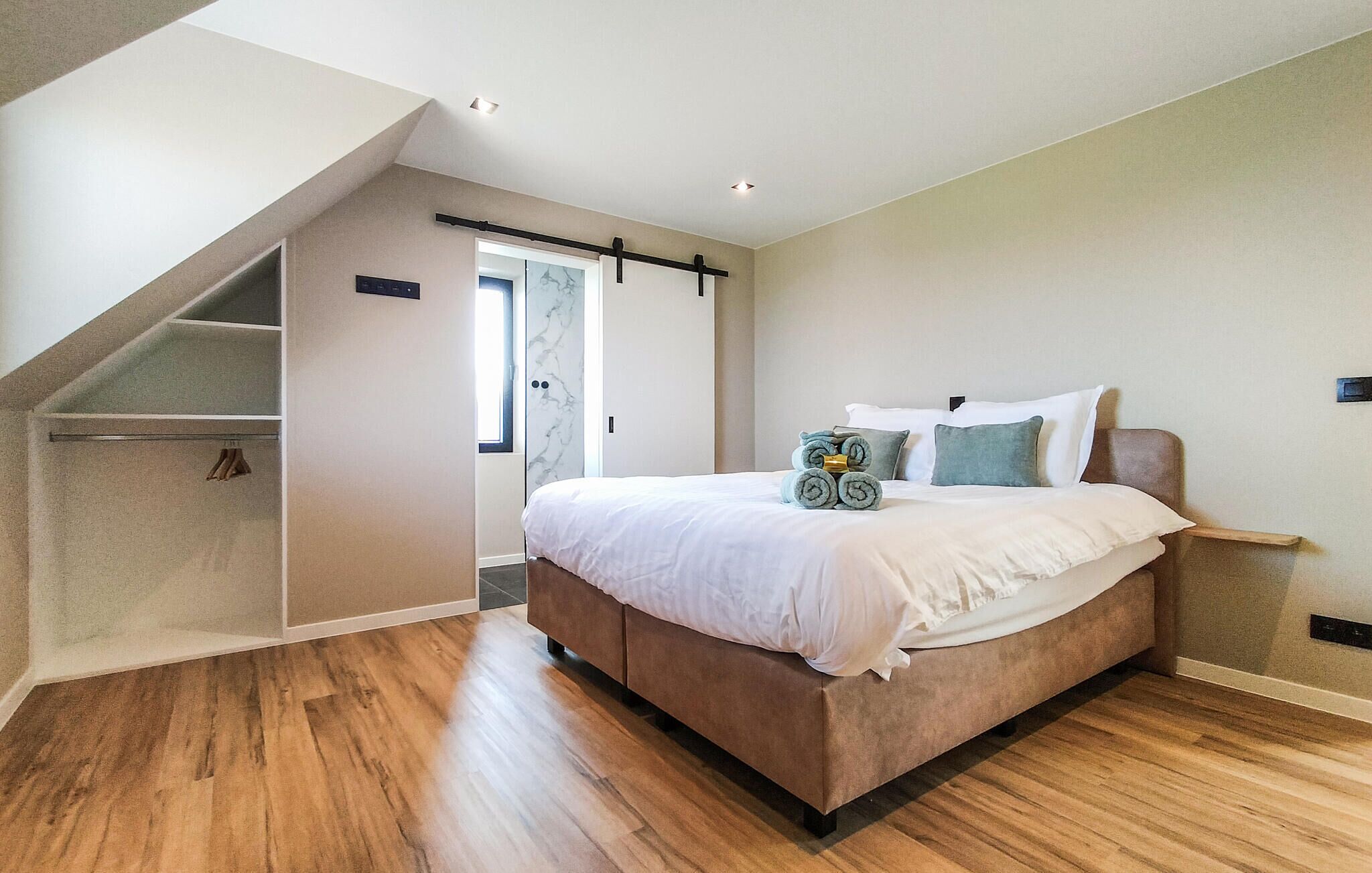 Un dormitorio con cama, piso de madera, armario y puerta que da a un balcón.