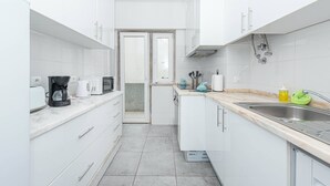 Una cocina moderna con armarios blancos, un lavamanos de acero inoxidable y una cafetera.