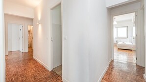 Un pasillo con piso de madera que conduce a un dormitorio con cama y mesita de noche.