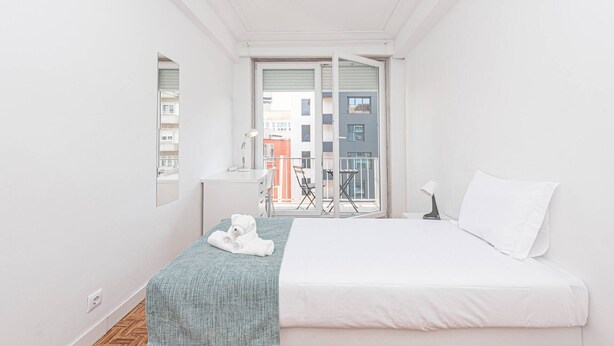 Un dormitorio con cama, un escritorio pequeño, una silla, una ventana y un balcón.