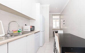 Une cuisine moderne avec des meubles blancs, un évier en acier inoxydable, un four à micro-ondes et un réfrigérateur.