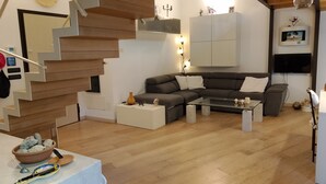 A modern living room with a wooden staircase, a grey sofa, a glass coffee table, and a flat-screen TV mounted on the wall. - Casa di A.L.A. by case al lago (Desenzano del Garda)