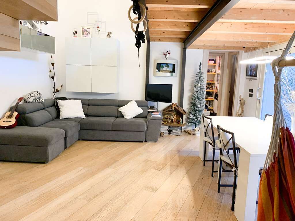 A cozy living room with a grey sectional sofa, a small dining table with chairs, a TV, and a Christmas tree.