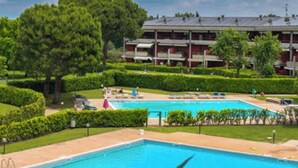 Una piscina rodeada de céspedes cuidados y un edificio de varios pisos con balcones.