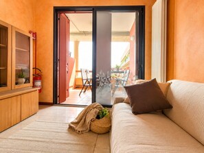 Ein modernes Wohnzimmer mit einer Couch, einer kleinen Kommode und einer Glastür, die zu einem Außenbereich führt.