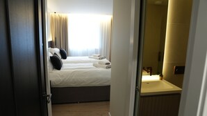 Una habitación de hotel con cama, mesita de noche, espejo y baño con lavamanos.