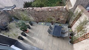 Una terraza en la azotea con piso de madera, mobiliario exterior, plantas en macetas y un muro de piedra.