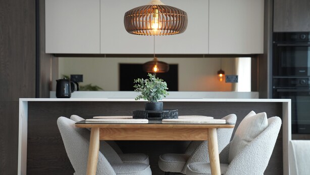 Una cocina moderna con una mesa de comedor de madera, sillas tapizadas en gris y una lámpara colgante.