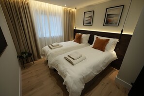 Habitación de hotel con dos camas, cortinas color beige, una mesita con una planta y obras de arte en la pared.