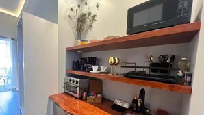Uma cozinha compacta com micro-ondas, forno e pia. Há prateleiras acima do balcão com diversos utensílios de cozinha.