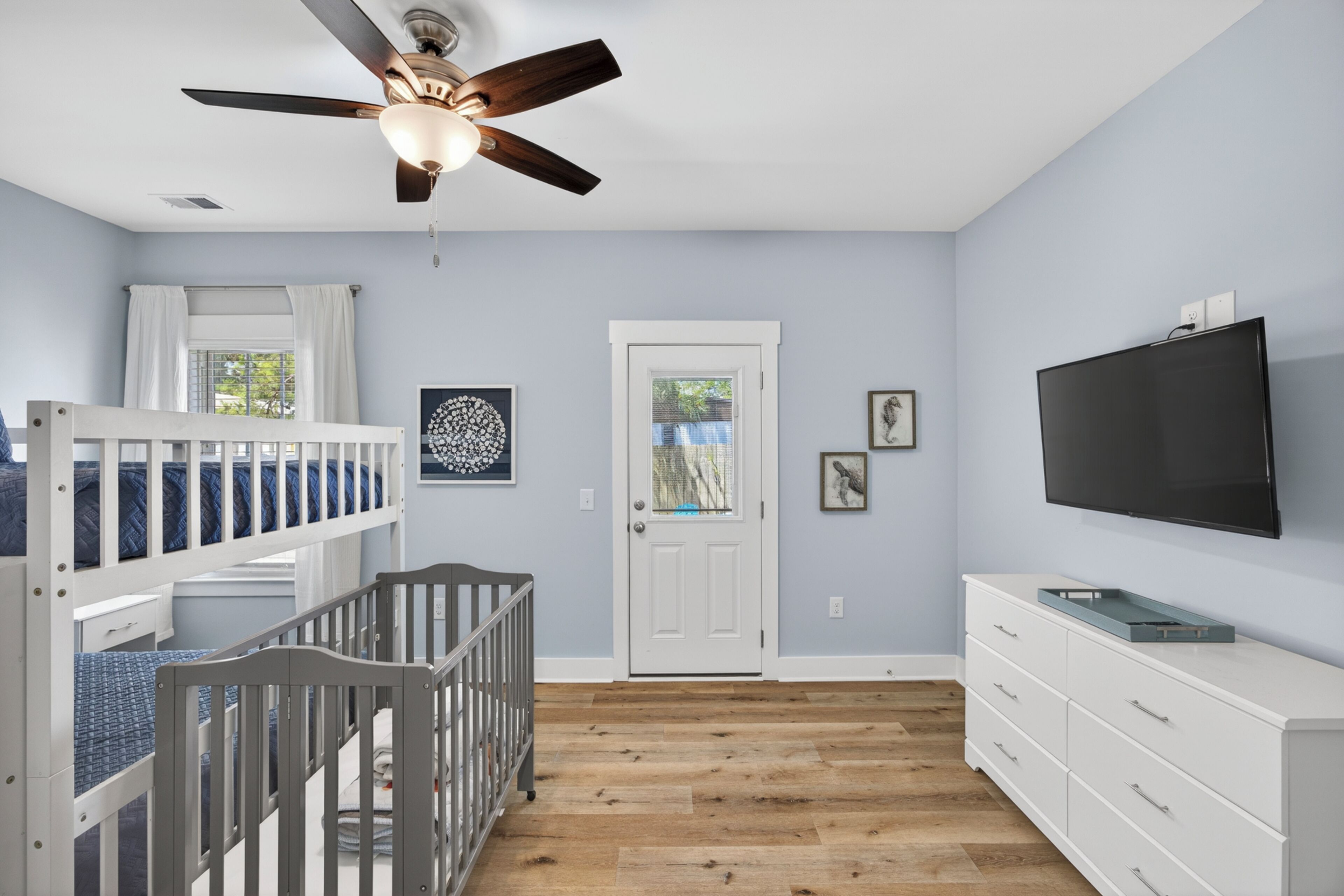 A room with bunk beds, a ceiling fan, a television, and a door with a window.