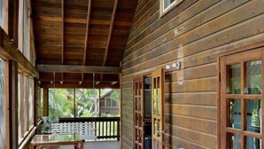 A wooden cabin with a covered porch, a white Adirondack chair, and a wooden bench.