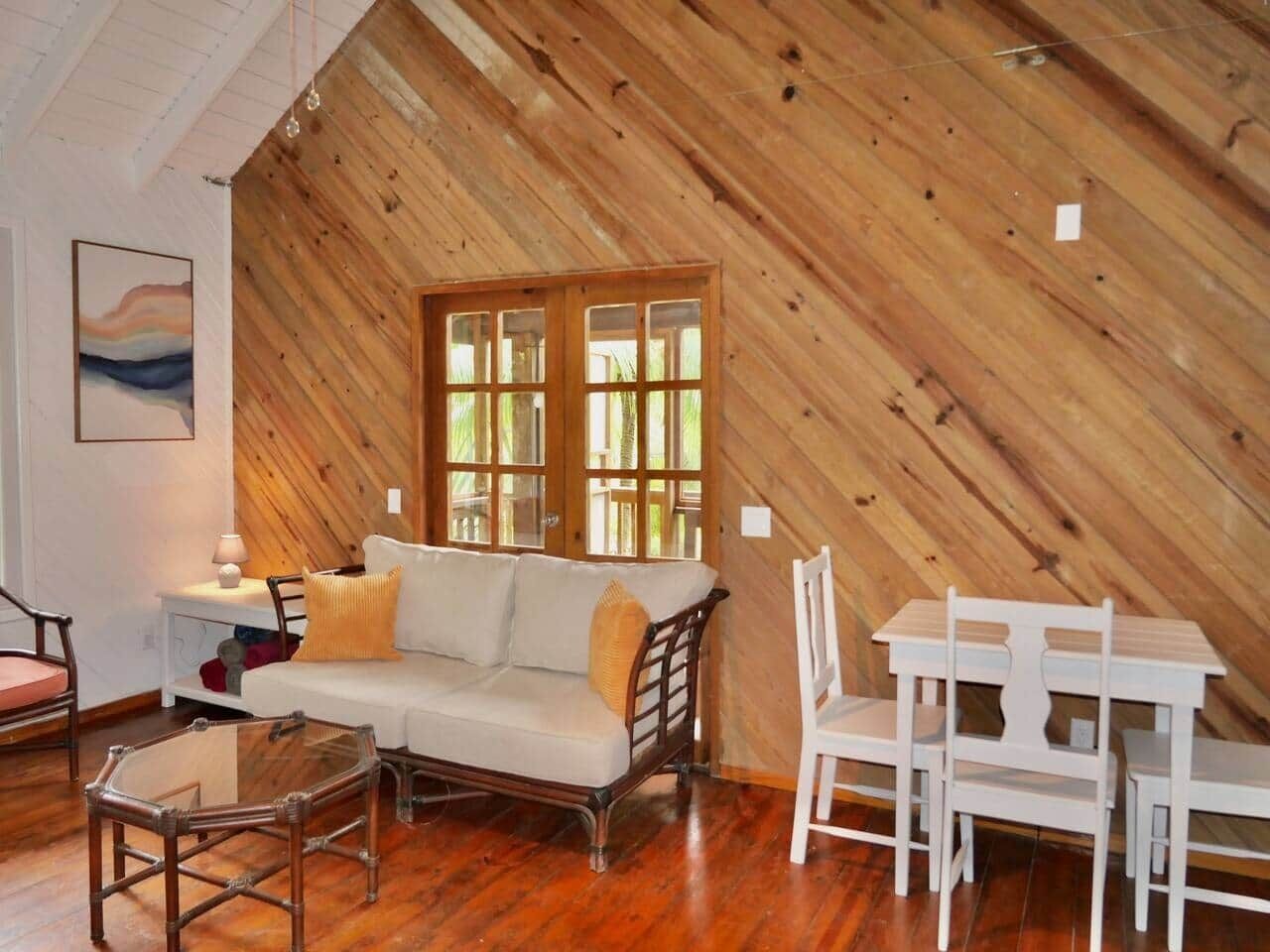 A cozy room with a wooden sloped ceiling, a white sofa, a small table, and a white chair.