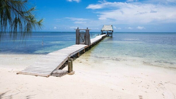 A wooden pier leading to a thatched-roof structure on a clear day. - Milton 2 Br Quiet Beachfront Pool Dock (José Santos Guardiola)