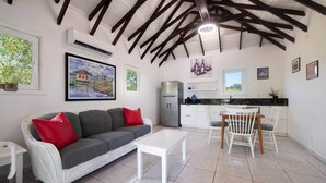 A modern living room with a sofa, dining table, and chairs. There is a kitchen area with a refrigerator and a window. - Milton 2 Br Quiet Beachfront Pool Dock (José Santos Guardiola)