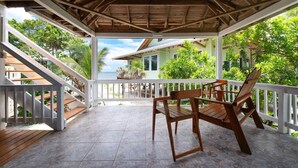 A covered outdoor area with a wooden deck, white railings, and a view of a house and greenery. - Milton 2 Br Quiet Beachfront Pool Dock (José Santos Guardiola)