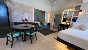 Une chambre d’hôtel moderne avec une table de salle à manger ronde, un canapé, un lit et un grand tableau abstrait accroché au mur.