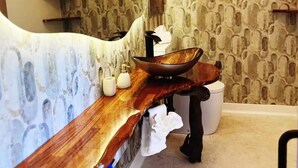 Une salle de bain avec un meuble-lavabo en bois, un grand miroir, un lavabo en forme de cuvette et un papier peint à motifs.