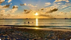 Une plage avec des bateaux et des gens dans l’eau au coucher du soleil.