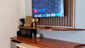 Une cuisine compacte avec un comptoir-bar en bois, deux tabourets, un four à micro-ondes et un téléviseur à écran plat fixé sur un mur recouvert de panneaux en bois.