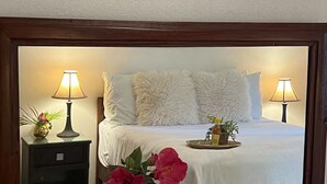 A hotel room with a bed, two bedside lamps, a nightstand, a tray with a bottle and a plant, and a vase with flowers. - Dover Apt #3, Beach 5 mins, St Lawrence Gap (Oistins)