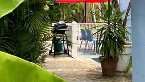 A patio area with a red umbrella, a grill, and potted plants. - Dover Apt #3, Beach 5 mins, St Lawrence Gap (Oistins)